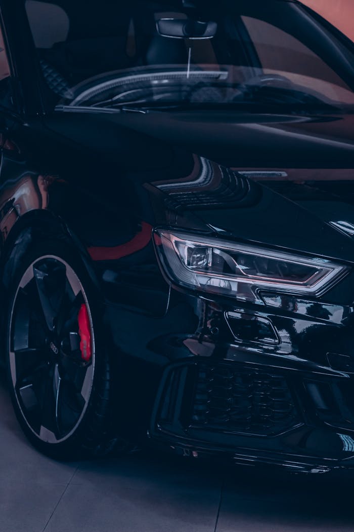 Close-up of a glossy black luxury car with prominent headlights reflecting light.